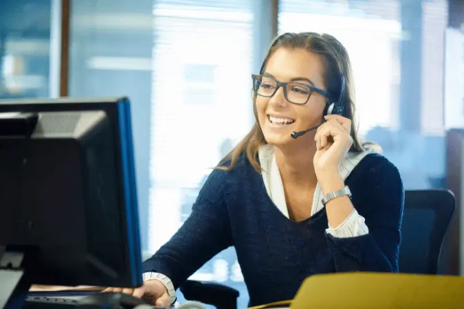 Smiling woman wearing a headset and glasses at her desk, early in her sales career.